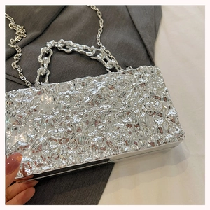 Detail view of the silver acrylic box bag with embossed texture and metal chain straps