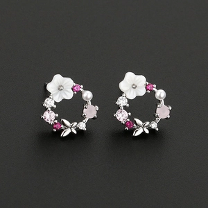 Close-up of floral hoop earrings with pink zircons, shell flower, and pearl on black background
