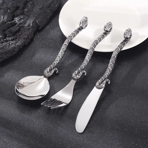 Close-up of three-piece silver cutlery set with detailed snake-shaped handles