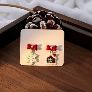 Asymmetric Christmas earrings with red bow, snowflake and gingerbread house on pine background