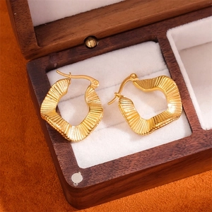 Golden titanium steel hoop earrings with irregular wave texture on a jewelry box