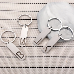 Polished stainless steel letter keychains with hollow alphabet tags on a textured background
