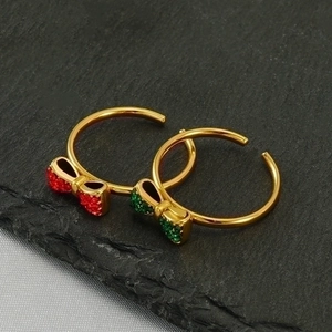 Detail of gold bow rings with red and green micro-pave crystals on dark stone