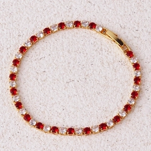 Detail of gold tennis bracelet featuring alternating red and clear zircon stones with clasp