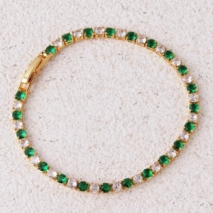 Close-up of golden tennis bracelet with inlaid green and white cubic zirconia stones