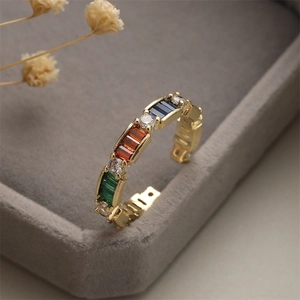 Detail of gold-plated open ring featuring multi-colored gemstones on a velvet box
