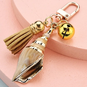 Close-up of conch shell keychain with gold bell, suede tassel and lobster clasp