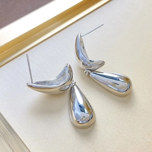 Minimalist silver teardrop metal stud earrings on a textured beige background