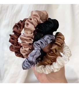 Primo piano di 6 eleganti elastici per capelli in raso in vari colori neutri tenuti in mano