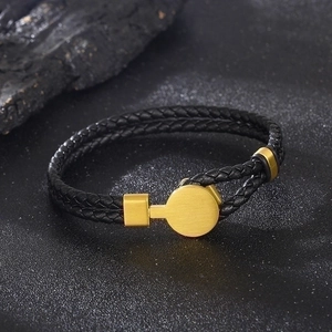 Macro detail of black braided leather bracelet with gold metal fastener on rock background