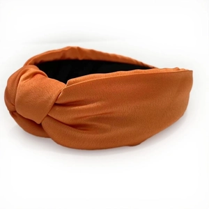Detail shot of a solid orange thickened satin wide headband with a top knot design