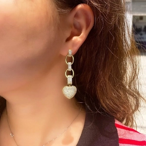 Elegant gold drop earrings with diamond-encrusted heart pendants worn by a model