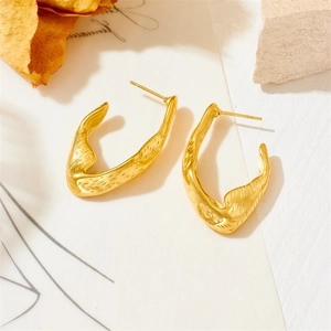 Macro detail of gold U-shaped earrings with textured matte finish on artistic background