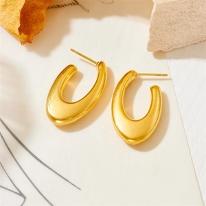 Detail shot of golden U-shaped geometric earrings on a minimalist textured surface