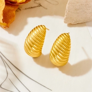 Macro detail of gold earrings featuring spiral texture and brushed metal finish