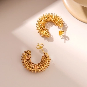 Golden hollow spring coil geometric earrings with spiral wrap design on beige background