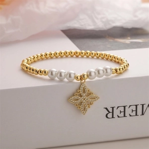 Macro shot of gold beaded bracelet with pearl accents and a zircon-encrusted flower charm
