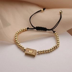 Close-up of a gold crown charm with zircon stones on an adjustable braided men's bracelet