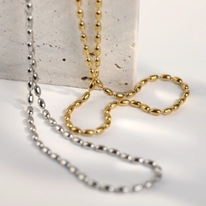 Minimalist gold and silver stainless steel rice bead chains on a textured stone base