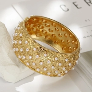 Detailed view of a wide gold-tone cuff bracelet with pearl inlay and hollow geometric patterns