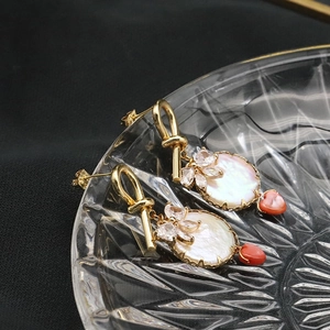 Detail of 18k gold earrings featuring mother of pearl, zircon flower and red heart pendant
