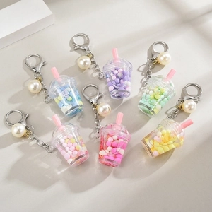 Quicksand bubble tea cup keychains with metal clasps and pearl charms on beige background