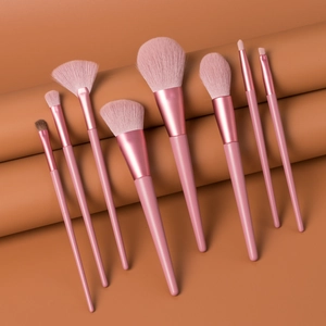 Detailed view of 8 pink makeup brushes with soft synthetic bristles on clay background