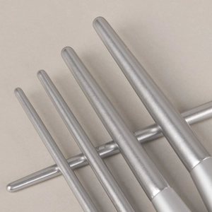 Close-up of five matte silver metal makeup brush handles on a beige background