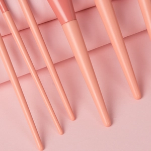 Close-up of coral pink makeup brush handles arranged diagonally on textured paper