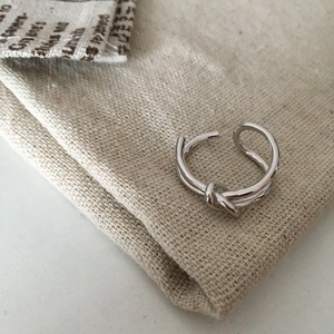Close-up of a silver irregular knot ring resting on a beige linen fabric bag background
