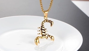 Detailed close-up of a 3D gold scorpion pendant on a metallic chain over white plate