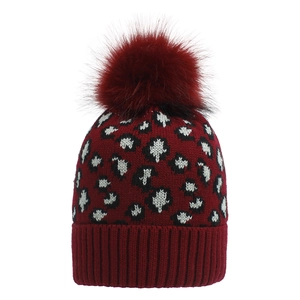 Close-up of red leopard pattern knit hat with large faux fur pom-pom detail