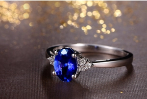 Macro shot of oval royal blue sapphire ring with side diamonds on a luxury dark background