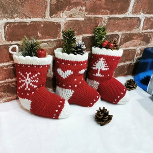 Three knitted Christmas stockings with snowflake and tree patterns on red brick background