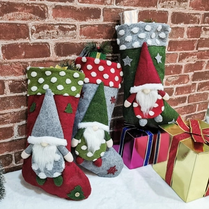 Three lamb wool Christmas stockings with gnome plush figurines on festive brick background