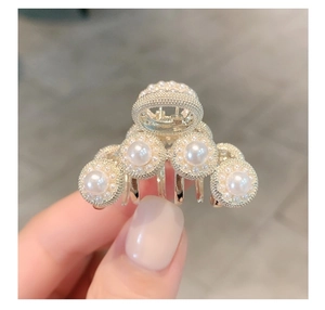Detailed close-up of a golden metal hair claw clip with elegant white pearls in crown shape