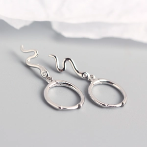 Macro shot of silver snake earrings with clear gemstone inlay and a polished metal hoop