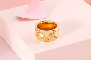 Detailed view of a wide gold stainless steel ring with stones on a pink display