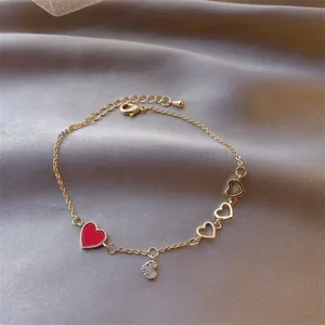 Close-up of gold chain bracelet with red enamel heart, crystal pavé heart, and extension link
