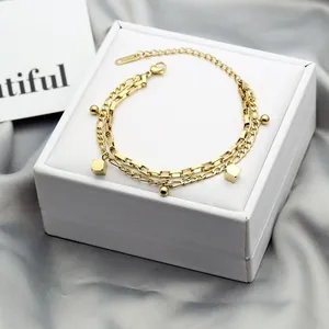 Detail of a gold-layered bracelet with geometric pendants on a white jewelry box