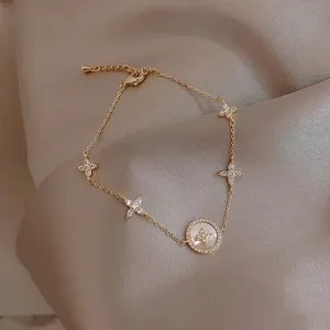 Close-up of golden clover bracelet with shimmering crystals and mother-of-pearl pendant