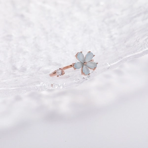 Macro shot of rose gold flower ring with blue petals and zircon on textured glass
