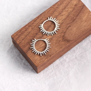 Detail of silver S925 sterling silver hoop earrings with sunburst bead design on wood