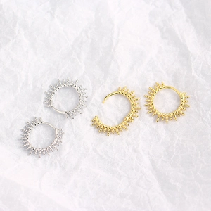 Artistic sunburst silver and gold earrings displayed on elegant white pleated paper