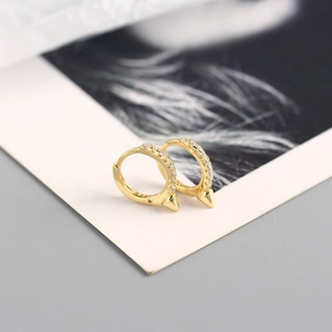 Détail de boucles d'oreilles huggies dorées avec zircons et pendentifs à pointe fine