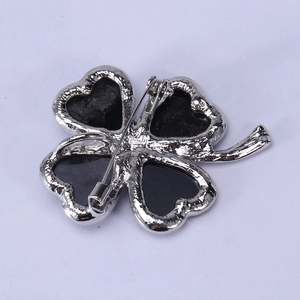 Silver four-leaf clover brooch with black shell inlay and pin clasp on white background