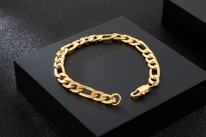 Detailed close-up of golden Figaro chain bracelet with lobster clasp on black background