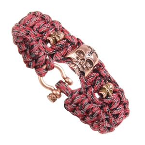 Detail of red and black paracord survival bracelet with bronze skull charms and shackle