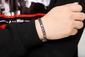 Detail shot of vintage stainless steel curb chain bracelet worn on wrist over black sleeve