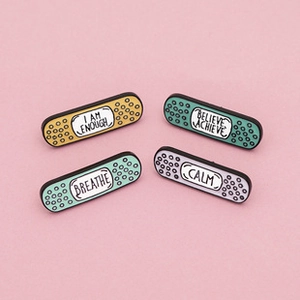 Detailed view of four colorful enamel band-aid pins with motivational phrases